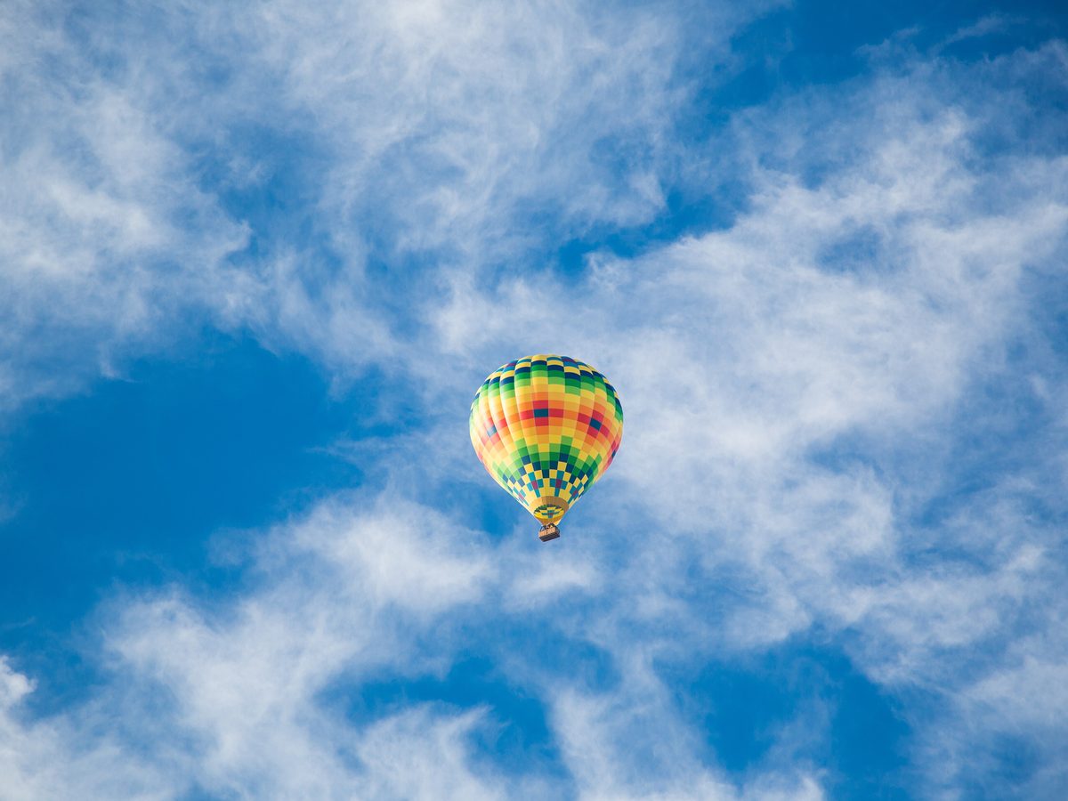 A colourful balloon high in a blue sky streaked with cloud