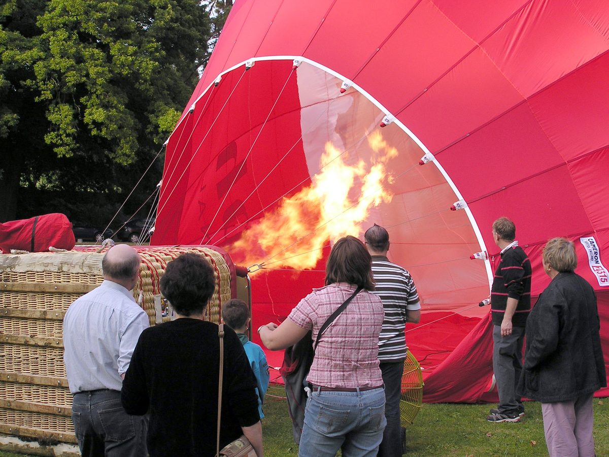 Ground crew and passengers watching a balloon envelope inflate, burner firing