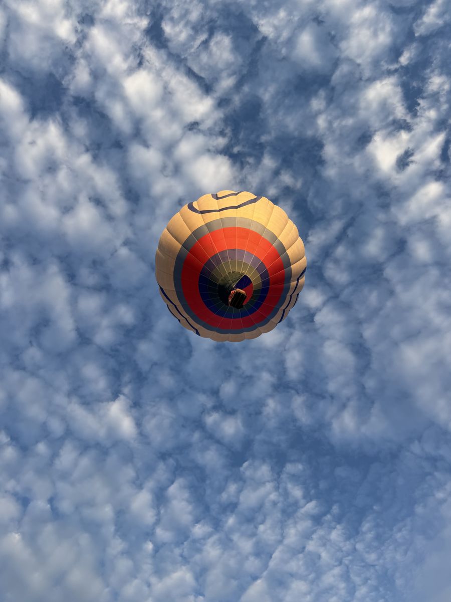 Looking straight up at a balloon against a sky of small puffy clouds
