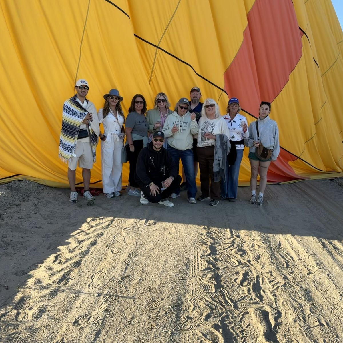 A group of passengers posing in front of a yellow and orange envelope laid out on the sand