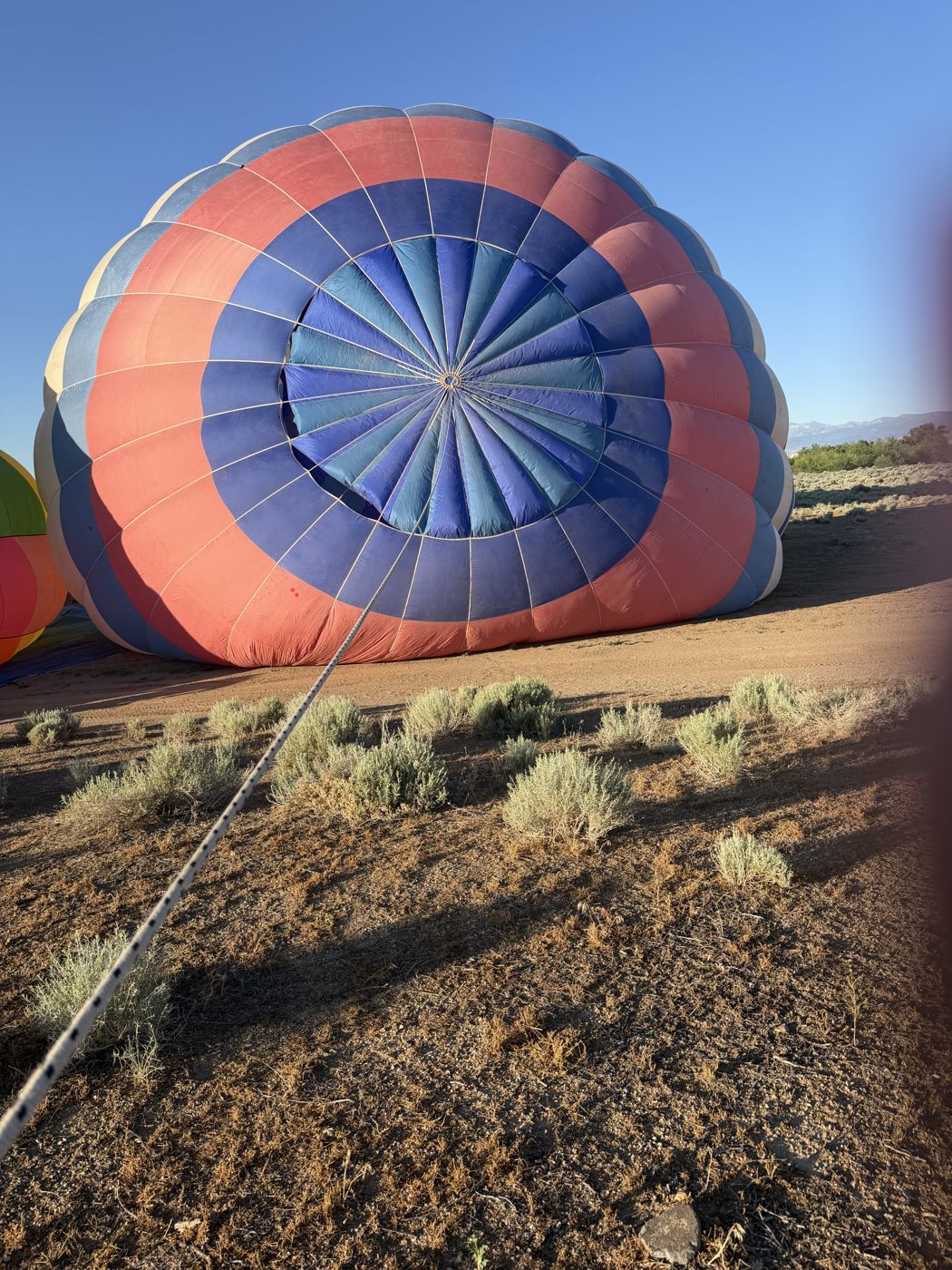 A red and blue balloon envelope half inflated on the ground, seen from the crown end