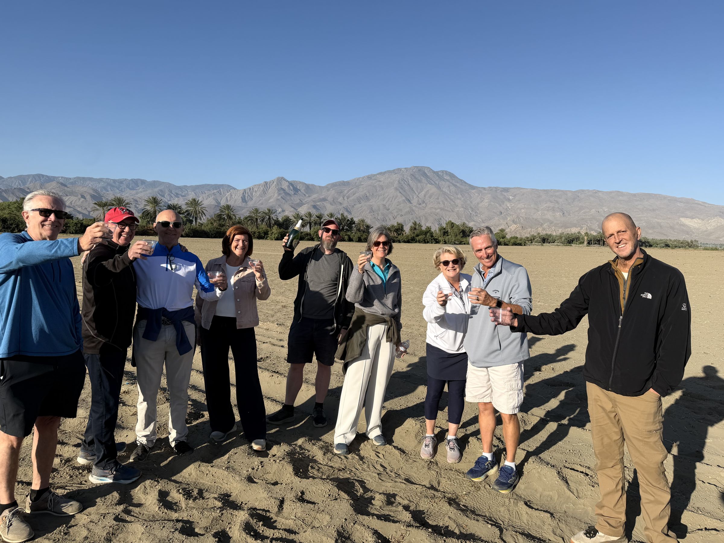 A group of passengers raising glasses in a post-flight toast, with mountains behind them