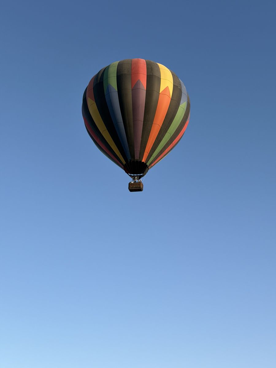 A rainbow-striped balloon high in a clear blue sky