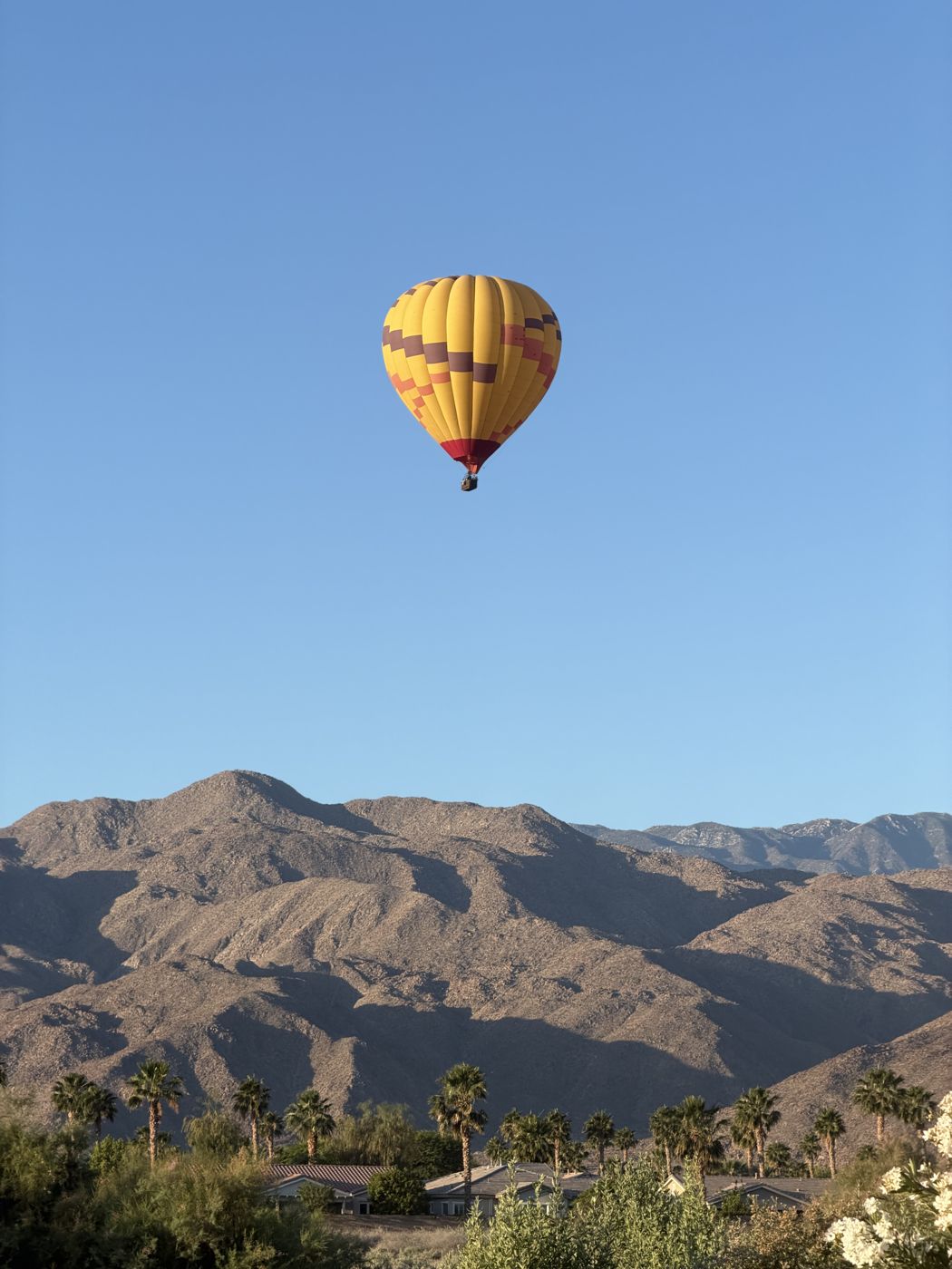 A yellow balloon floating above rugged desert mountains and palm trees